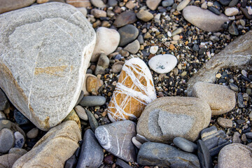 Pebble beach. Beautiful sea stones, different sizes and textures. With streaks, inclusions. On the beach after the storm, small objects and shell fragments were thrown out. Textured rocky background.