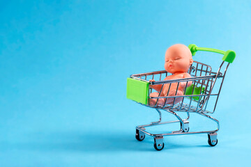 Doll sitting on a shopping cart on a blue background. Eco, surrogate motherhood, buy a child for...