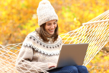 Happy woman using laptop sitting on hammock in fall