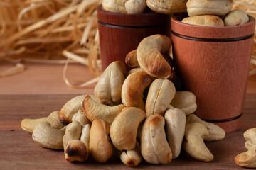 cashew nuts on a wooden table and in two wooden cups with straw background.