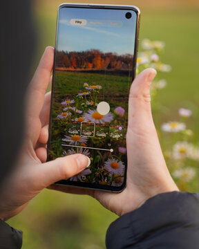 Osoba płci żeńskiej fotografuje naturę, jest to jesień a zdjęcie wykonuje telefonem kom&oacute;rkowym. 