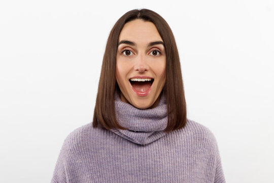 Studio shot of smiling glad woman has appealing appearance, smiles broadly, dressed purple sweater poses against white background expresses positive emotions likes what she sees, rejoices new purchase