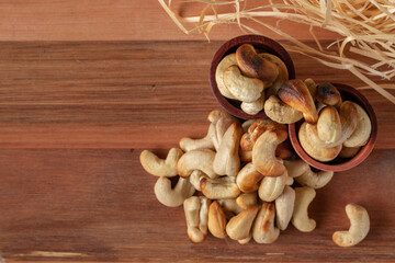 cashew nuts on a wooden table and in two wooden cups with straw background.