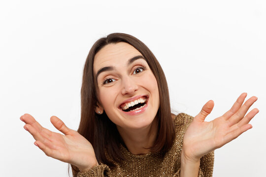 Excited young woman , casual in a golden sweater, screams happily, raises her hands up in surprise, over white studio wall with copy space. Sincere people emotions.