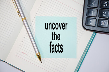 text uncover the facts written on a blue sticker glued to a notebook next to a calculator and a pen