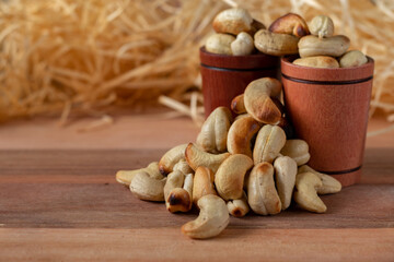 cashew nuts on a wooden table and in two wooden cups with straw background.