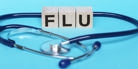 Wooden block form the word FLU with stethoscope on on light blue background. Medical and health care concept.