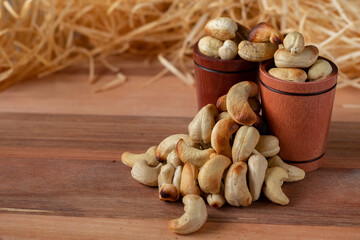cashew nuts on a wooden table and in two wooden cups with straw background.
