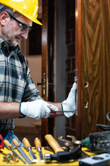 Close-up. Carpenter at work repairs and installs the new lock of a wooden door. Construction...