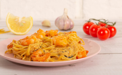 Spaghetti with shrimps with ingredients on a light background in a pink plate. Spaghetti, tomatoes, garlic, lemon. Side view. Selective focus