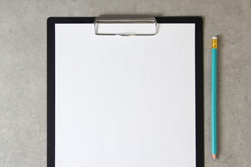 Template of white paper with simple pencil on light grey concrete background in a black tablet with a clip. Concept of new idea, business plan and strategy, empty space for text