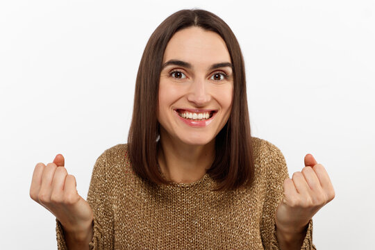 Excited young woman , casual in a golden sweater, screams happily, raises her hands up in surprise, over white studio wall with copy space. Sincere people emotions.