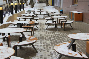 Tables and benches covered with snow stand on the city street on a pavement next to the restaurant McDonald's winter in Russia