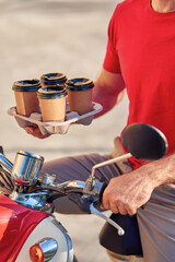Male courier delivering coffee on scooter, selective focus on four paper cups