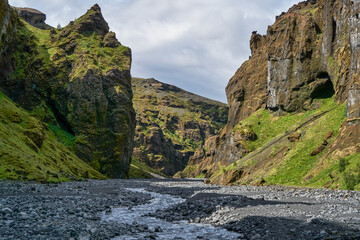 A narrow canyon carved by the Stakkholtsgjá River in Þórsmörk, Iceland, features towering moss-covered cliffs and a rocky streambed.