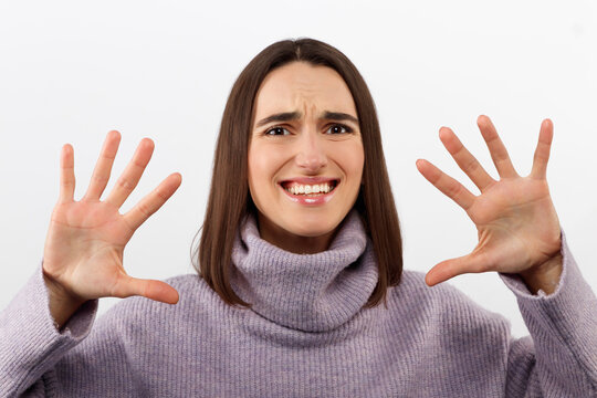 Clueless satisfied young female has spreads hands with hesitation, can not make choice between two nice products, feels doubtful, wears red loose clothes, isolated over white background.