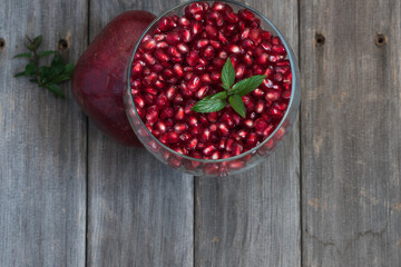 Fresh pomegranate arils with mint leaves in a glass bowl on a weathered board table top.