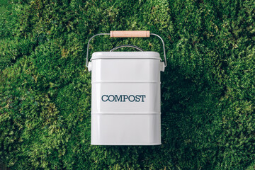 Trash bin for composting with leftover from kitchen on green grass, moss background. Top view. Copy...