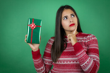 Young beautiful girl holding gift over isolated white background thinking and looking to the side