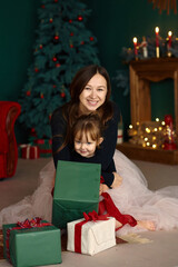 Fototapeta na wymiar Portrait of a young mother with her little daughter having fun and opening Christmas presents.