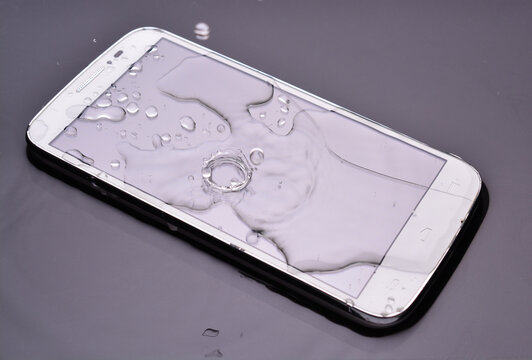 White Smartphone Dropped Into A Puddle Of Water Cracked Screen From Above Dripping Water Drops, Rain.