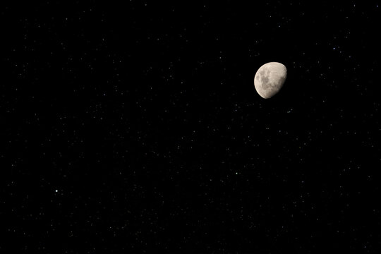 Foto de la luna, en cuarto creciente con estrellas en el cielo.