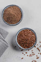 Brown flax seed and ground or crushed flaxseed or linseed in small bowl on light gray background.