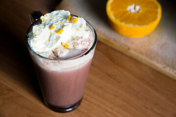 a glass of hot cocoa with whipped cream and orange on the kitchen wooden table