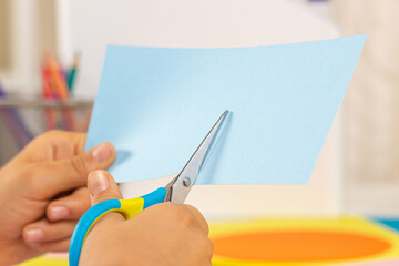 Kid hands cutting colored paper with scissors. Education, learning, paper craft, entertainment at home