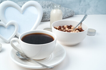 Obraz premium Breakfast on a romantic background, coffee, cereal balls, milk, heart-shaped frame and scarf on a white-gray background. Concept February 14.