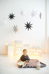 Little toddler girl sitting with a book in her hands on a knitted carpet on the floor.