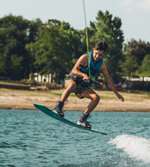 young man doing wakeboarding in a lake whit mountains also doing jumps