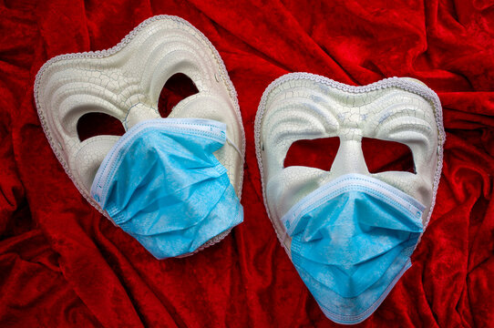 Coronavirus Impact On Theatre And The Performing Arts And The Covid-19 Response Is Theater Concept With The Comedy Mask And The One For Tragedy Wearing Protection Face Masks On Red Velvet Background