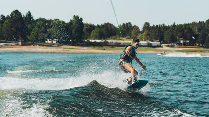 young man doing wakeboarding in a lake whit mountains also doing jumps