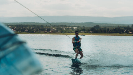 young man doing wakeboarding in a lake whit mountains also doing jumps