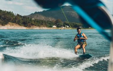 young man doing wakeboarding in a lake whit mountains also doing jumps