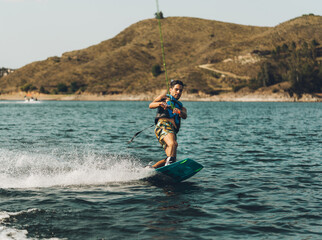 young man doing wakeboarding in a lake whit mountains also doing jumps