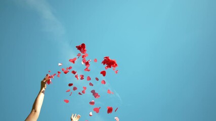SLOW MOTION, BOTTOM UP: Unrecognizable person throws a handful of red confetti into the sky during a Valentine's day celebration. Woman tosses red heart shaped papers in air during baby gender reveal - Powered by Adobe