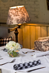 Restaurant table setting with warm lamp in the background and white roses. Warm interior decoration