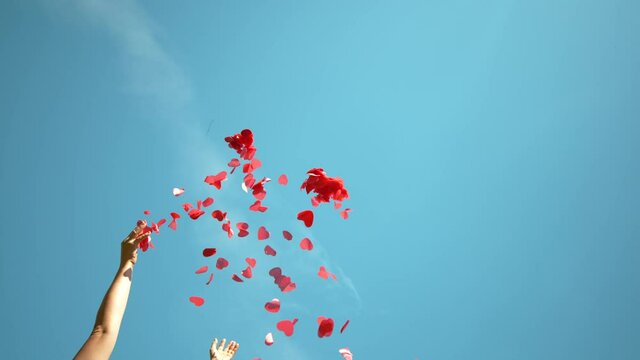 SLOW MOTION, BOTTOM UP: Unrecognizable person throws a handful of red confetti into the sky during a Valentine's day celebration. Woman tosses red heart shaped papers in air during baby gender reveal