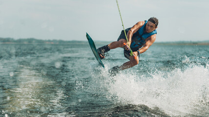 young man doing wakeboarding in a lake whit mountains also doing jumps - obrazy, fototapety, plakaty