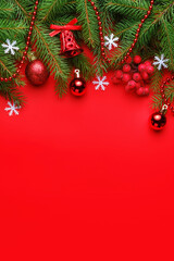 Fototapeta na wymiar Top view of Christmas composition with spruce branches, snowflakes, balls, red berries and bell on red background. Christmas background concept, vertical orientation, copy space