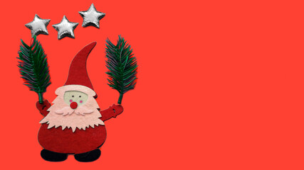 Handmade Christmas composition. A drawing of Santa Claus, in his hands he is holding fir branches, above his head are three silver stars made of glued pieces of felt and plywood on a red background.