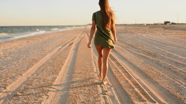 sexy tender sensual erotic young skinny woman walks on the beach along the seashore. A woman in a shirt and thong bikini panties with a bare booty. ocean lifestyle