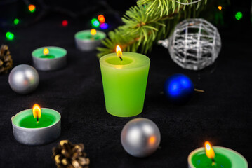 Green candles next to the christmas tree, lights and holiday decoration. Merry Christmas or Happy New Year greeting card.