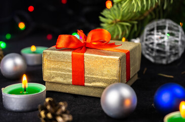 Golden present gift box with red ribbon next to the christmas tree, candles and holiday decoration. Merry Christmas or Happy New Year greeting card.