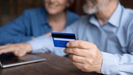 Close up mature man holding plastic credit card, senior couple family paying online, using laptop, satisfied older customers making secure internet payment, shopping, browsing banking service