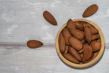 Almonds in a wooden bowl on a white wooden table. Close-up and minimalist shot. top view
