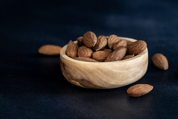 Almonds in a wooden bowl with a wooden spoon on a black table. Close-up and minimalist shot. Eco friendly concept