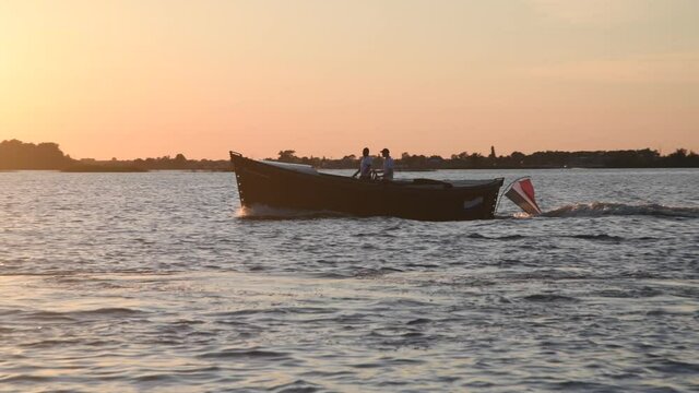 A small recreational boat passing by on a lake during sunset in summer
